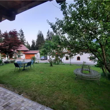 Ein schöner Garten mit viel Grün und einem Tisch mit Stühlen. Im Hintergrund sind einige Häuser und Bäume zu sehen.