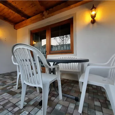 Ein gemütlicher Außenbereich mit einem Tisch und zwei Stühlen. Die Wände sind hell, und es gibt Wandlampen, die eine angenehme Atmosphäre schaffen.