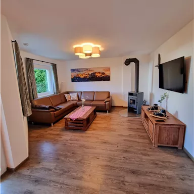 Ein gemütliches Wohnzimmer mit einer bequemen Couch und einem modernen Fernseher. Der Holzfußboden und der Kamin verleihen dem Raum eine warme Atmosphäre.