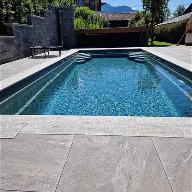 Ein stilvoller Pool mit klarem, blauem Wasser in einem modernen Garten. Umgeben von Natur und einer ansprechenden Terrassenfläche.