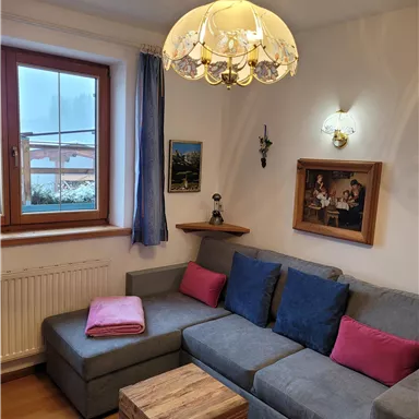 Ein gemütliches Wohnzimmer mit einem grauen Sofa und bunten Kissen. Es gibt ein Holztablett und Bilder an der Wand.