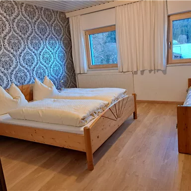 Ein gemütliches Schlafzimmer mit zwei Holzbetten und einem Fenster, das Blick auf die Natur bietet. Die Wände sind mit einem eleganten Muster dekoriert.