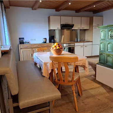 Eine gemütliche Küche mit einem Holzofen und einem Esstisch. Auf dem Tisch steht eine Schüssel mit frischem Obst.