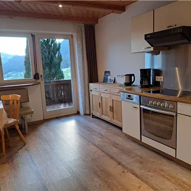 Eine moderne Küche mit Holzdetails und einem Fenster, das einen Blick auf die Berge bietet. Der Raum ist hell und einladend, mit einem kleinen Esstisch und Stühlen.