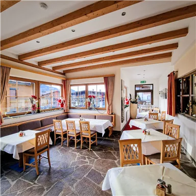 An inviting restaurant with large windows and a wooden beam ceiling. The tables are elegantly set and there is a cozy atmosphere.