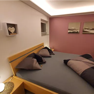 Ein stilvolles Schlafzimmer mit einem Doppelbett und dekorativen Kissen. Die Wände sind in sanften Farben gehalten, mit Bildern und modernen Regalen.