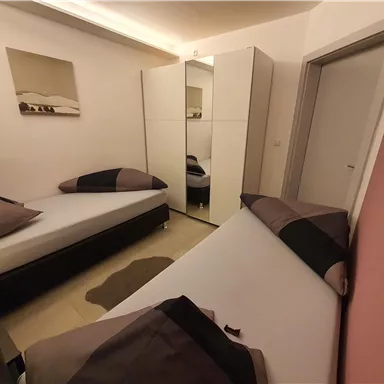 Ein einfaches Schlafzimmer mit zwei Einzelbetten und einem modernen Kleiderschrank. Die Wände sind in sanften Farben gestrichen, und es gibt ein Bild an der Wand.