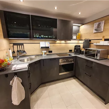 Moderne Küche mit dunklen Schränken und hellen Wänden. Auf der Arbeitsfläche stehen Küchenutensilien und frisches Obst.