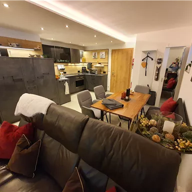 Eine moderne und gemütliche Wohnküche mit einem Esstisch und Stühlen. Der Raum ist hell erleuchtet und gemütlich eingerichtet.