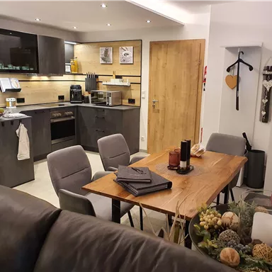 Moderne Küche mit einem Esstisch und Stühlen. Das Design ist schlicht und elegant, mit warmen Farben und gut angeordneten Möbeln.