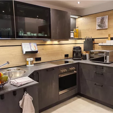 Eine moderne Küche mit grauen Möbeln und Holzdetails. Sie ist mit verschiedenen Geräten wie einem Herd, einer Mikrowelle und einem Spülbecken ausgestattet.