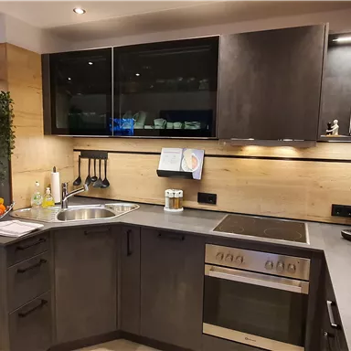 Eine moderne Küche mit dunklen Möbeln und Holzakzenten. Der Raum ist gut beleuchtet und enthält eine Spüle, einen Herd und frisches Obst auf der Arbeitsplatte.