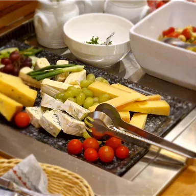 A buffet with various types of cheese, grapes, and cherry tomatoes. In the background, there is a bowl of salad.