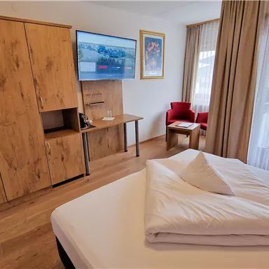 A cozy hotel room with wooden cabinets and a television on the wall. There is also a small living area with a red chair.