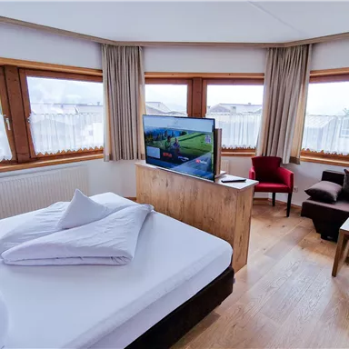 A bright room with large windows and a view of the surroundings. The room is equipped with a bed, a sofa, and a television.