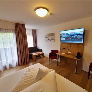 A modern hotel room with a double bed, a television, and a table. Large windows let in plenty of light and offer a pleasant view.