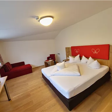 A modern hotel room with a large bed and several pillows. A cozy armchair and a television complete the furnishings.