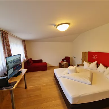 A cozy hotel room with a large double bed and several pillows. There is a television and a seating area with a sofa.