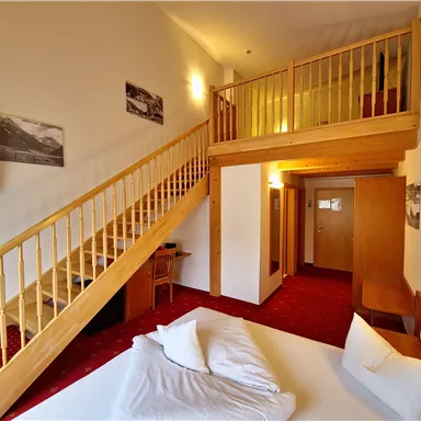 A cozy hotel room with an open upper floor. The staircase leads to an additional sleeping area and the room is bright and inviting.