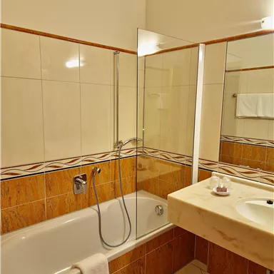 A modern bathroom with a bathtub and a shower. The walls are brightly tiled and feature a decorative border.