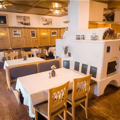 A cozy restaurant with wooden-paneled walls and white tables. In the center stands a traditional fireplace.