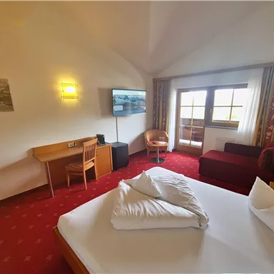 A cozy hotel room with a large bed, a television, and a desk. The decor is simple and inviting, with a view of nature through the window.