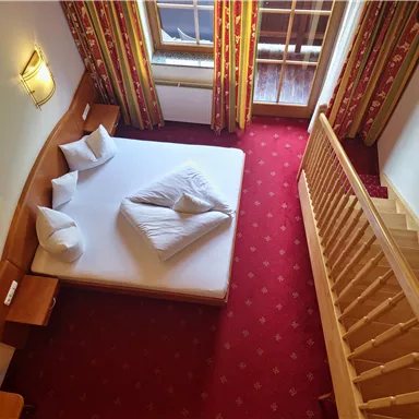 A cozy room with a double bed and two pillows. The room has large windows and access to the staircase.