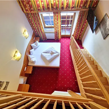 A cozy room with a double bed and bright curtains. A wooden staircase leads to the upper floor.