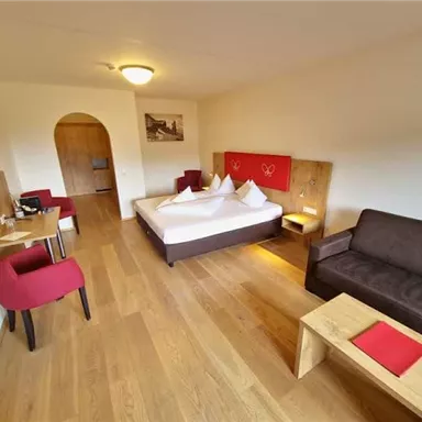 A cozy hotel room with a large bed, a sofa, and a table. The room has wooden floors and warm colors.