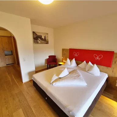 A cozy bedroom with a large bed and wooden flooring. The walls are bright and the room is simply but stylishly furnished.