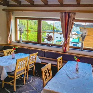 A cozy dining room with wooden chairs and tables covered with white tablecloths. Large windows offer a view of nature and the peaceful surroundings.