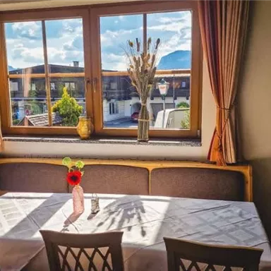 A cozy table in a restaurant with a window view of the mountains. On the table is a small flower vase with a red flower.