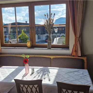 An inviting restaurant with a table and chairs, decorated with a flower vase. Through the large windows, you can see the mountains and a bright, friendly atmosphere.