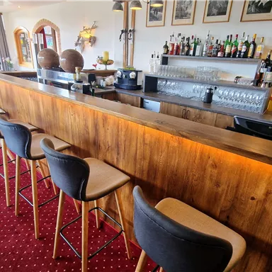 A modern bar with a wooden counter and seating. In the background, there are shelves with drinks and a cozy atmosphere.
