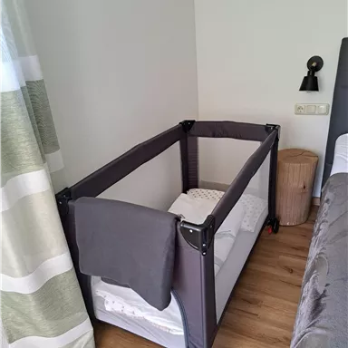 A children's bed in a modern bedroom. The bed is equipped with a blanket and is next to a bed and a bedside table.