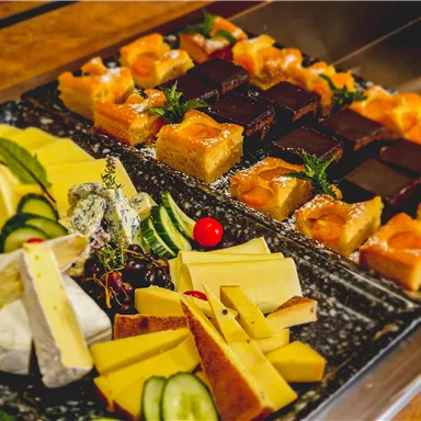 A delicious arrangement of various types of cheese and sweet desserts. The platter is decorated with fresh herbs and fruit.
