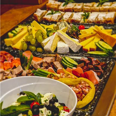 A rich selection of cheese, sausage, and fresh vegetables. In the foreground, there is a bowl of colorful salad.