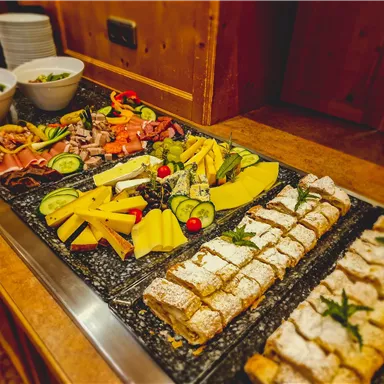 A lovingly arranged buffet with various types of cheese, ham, fresh fruit, and vegetables. On the right side, you can see a sweet dessert.
