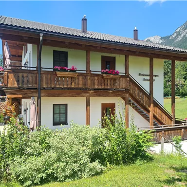 Ein gemütliches Holzhaus mit zwei Etagen und Balkonen. Es liegt in einer ruhigen grünen Umgebung mit Blick auf die Berge.
