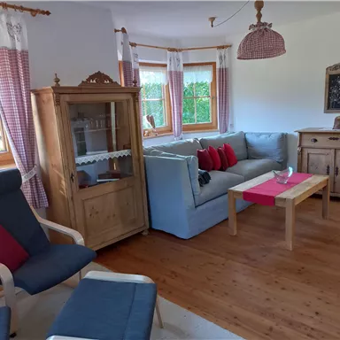 Eine gemütliche Wohnzimmercouch mit roten Kissen und einem Holztisch. Das Zimmer ist hell und einladend, mit großen Fenstern und Holzmöbeln.