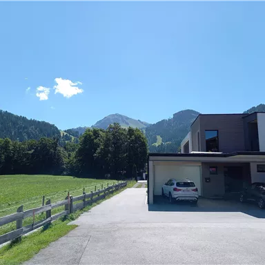 A modern house with garage access in a rural setting. In the background, mountains and a bright blue sky can be seen.