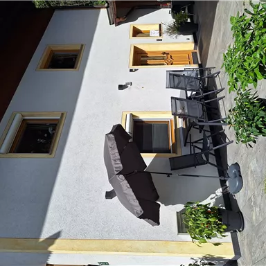 Ein schönes Haus mit einer Terrasse und modernen Sitzmöbeln. Der Garten ist grün und gepflegt mit zahlreichen Pflanzen.