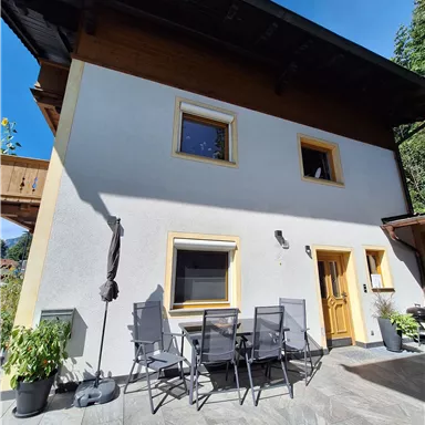 Ein modernes Haus mit einer Terrasse und Sitzgelegenheiten. Die Fassade ist hell und hat große Fenster.