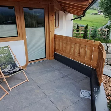 A cozy balcony with two loungers and a view of the surrounding nature. The wooden cladding and the plants create an inviting atmosphere.