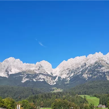 An impressive mountain landscape under a clear blue sky. A signpost points to various hiking destinations.
