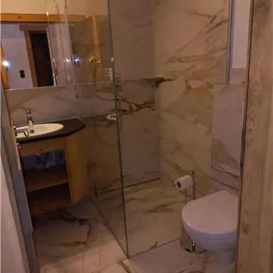 Ein modernes Badezimmer mit eleganten Marmorfliesen. Es gibt eine gläserne Dusche, ein Waschbecken und eine Toilette.