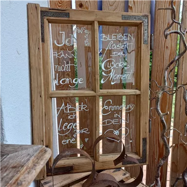 Ein kreatives Holzfenster mit handgeschriebenen Texten, die Erinnerungen und den Genuss des Augenblicks thematisieren. Es ist rustikal und verleiht dem Raum eine persönliche Note.