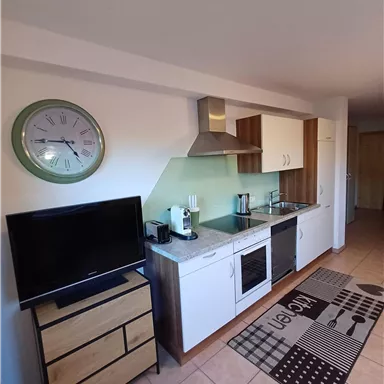 Eine moderne Küche mit einem Herd, einem Kühlschrank und einem kleinen Fernseher. Der Raum hat ein einfaches, aber elegantes Design und einen Teppich in neutralen Farben.