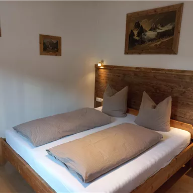 Ein gemütliches Schlafzimmer mit einem Doppelbett und weichen Kissen. An den Wänden hängen einige Bilder, die eine warme Atmosphäre schaffen.