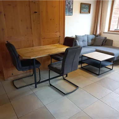 Ein gemütlicher Wohnbereich mit einem Holzstudiotisch und stilvollen Stühlen. Eine graue Couch und ein Beistelltisch befinden sich ebenfalls im Raum.